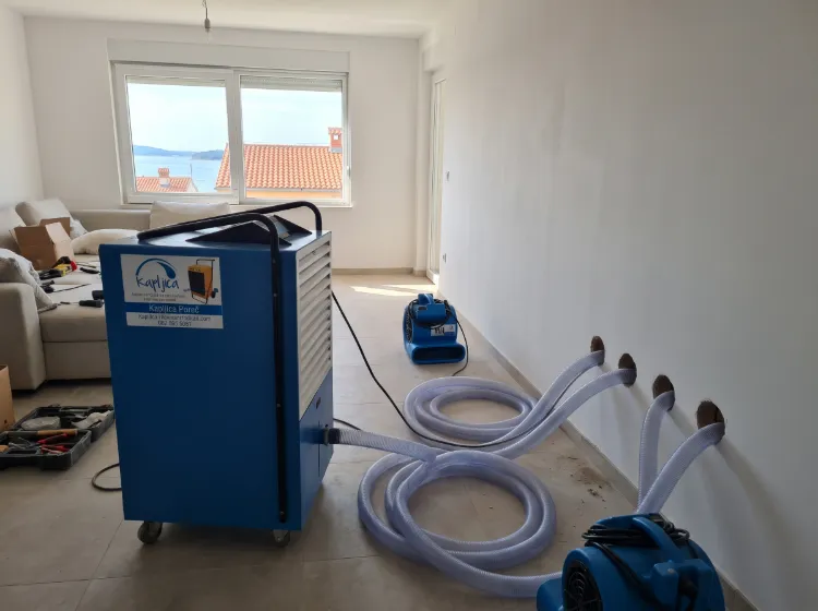 Sustav plastičnih cijevi spojen na plavi isušivač zraka koji usmjerava zrak u unutrašnjost zida